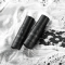 Lash and Brow Shampoos lying down on a black surface, a great amount of white foam surrounds the product